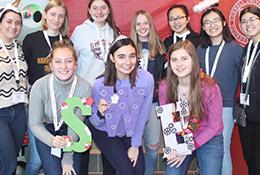 Members of the Society of Women Engineers at Cornell stand smiling in a group with homemade giant letters "SWE"