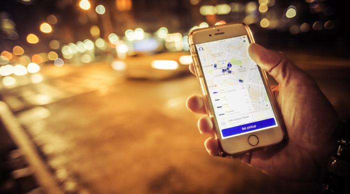 image of hand holding phone with ride sharing app in front of city street at night