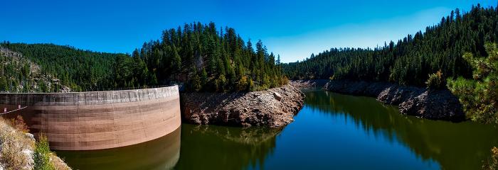 image of dam with blue water and sky with trees in background