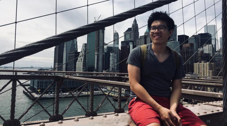 Bill Wu sitting on a bridge with a city skyline in background