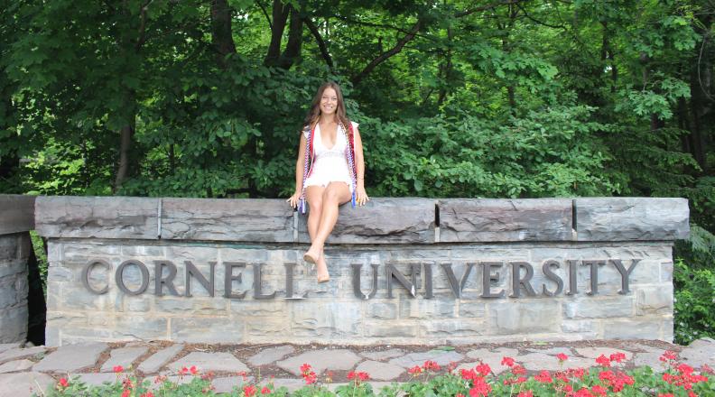 Rebecca Holstein sitting on wall that reads Cornell University